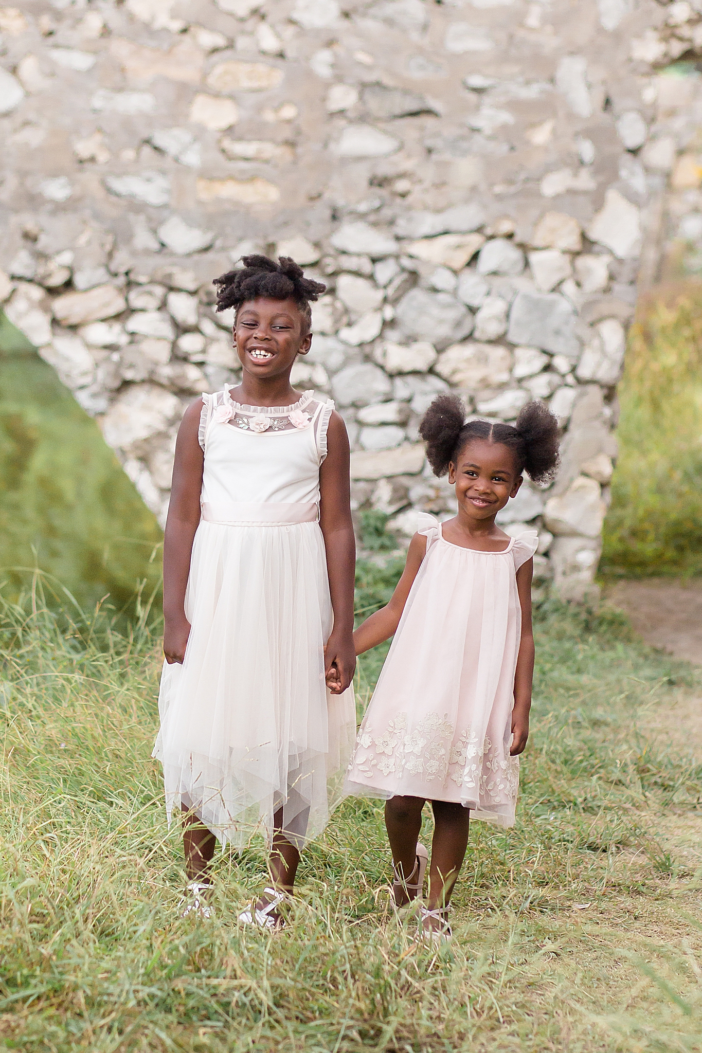 sisters hold hands in front of stone bridge during McKinney family portraits