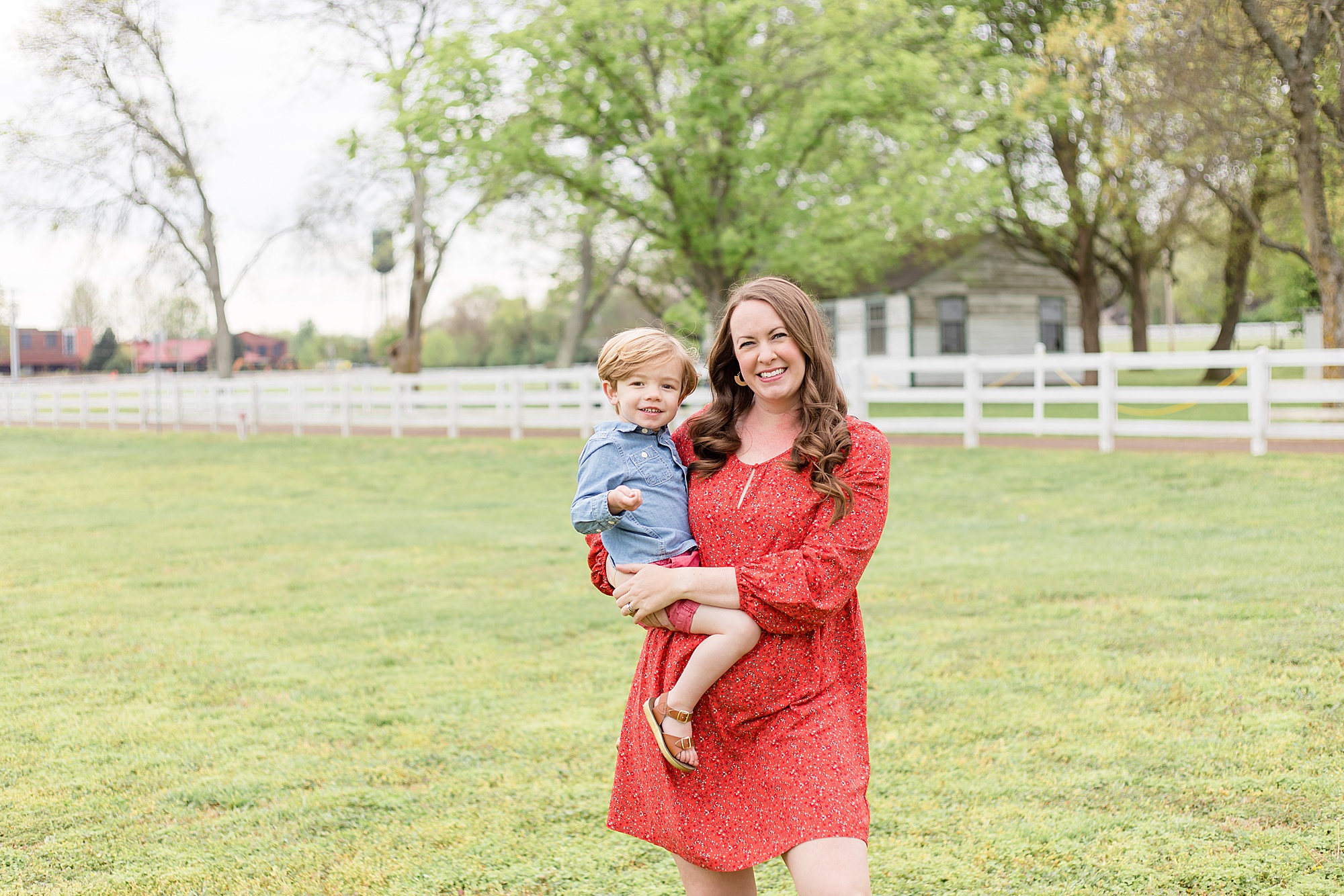 Mom in red dress holds son in front of white picket fence at Harlinsdale Farm with Franklin family photographer Wisp + Willow Photography Co. 