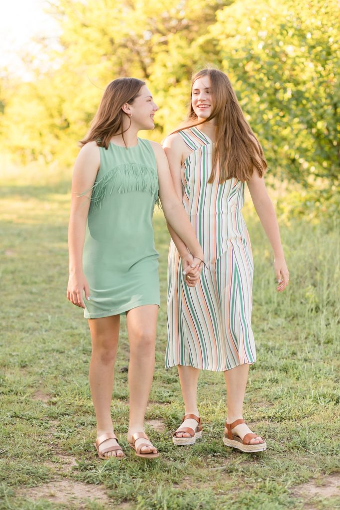 sisters walk in grassy field together during spring family portrait session with wisp + willow photography co.