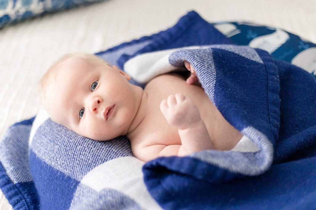 boy lays on bed in blue plaid blanket for lifestyle newborn session with Wisp + Willow Photography Co. 