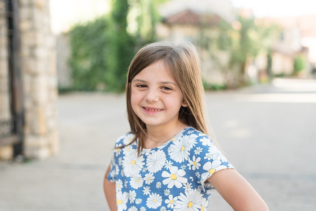 little girl in blue dress with white flowers smiles for camera during family portrait session with Adriatica Village photographer Wisp + Willow Photography Co. 