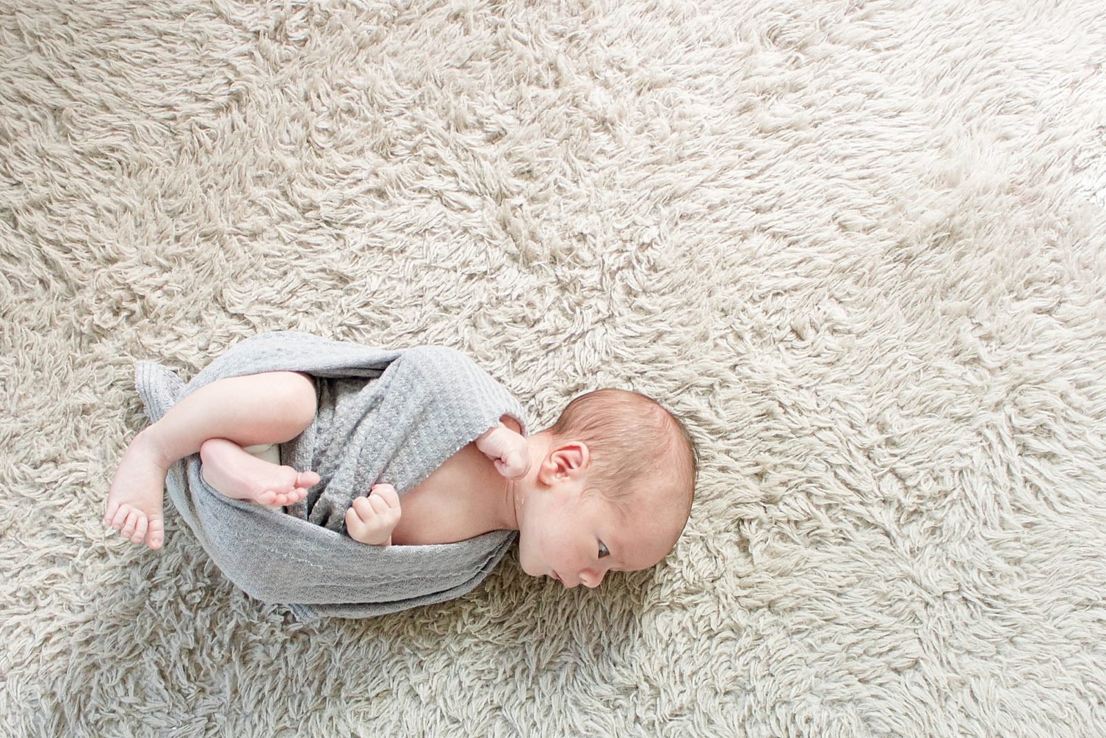 Newborn baby lays in baby wrap on carpet in nursery during lifestyle session with Brentwood family photographer Wisp + Willow Photography Co. 
