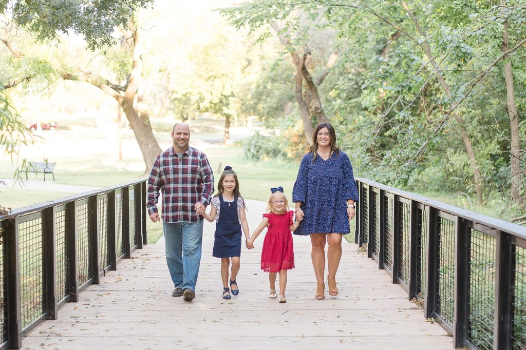 Family of 4 walks on bridge at Finch Park during fall mini session with McKinney photographer Wisp + Willow Photography Co. 