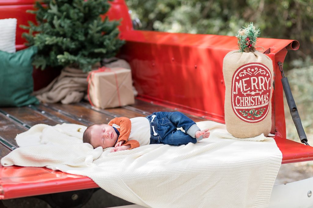newborn baby boy lays on bed of truck during red truck christmas mini sessions