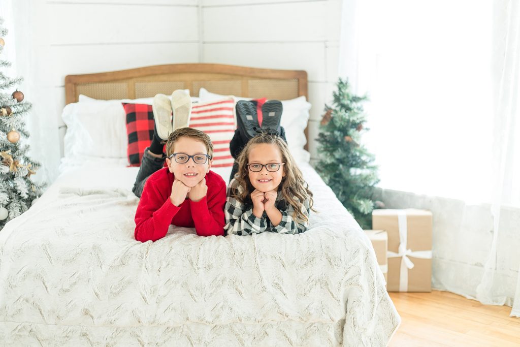 siblings pose on bed during Christmas minis with McKinney mini sessions photographer Wisp + Willow Photography Co. 