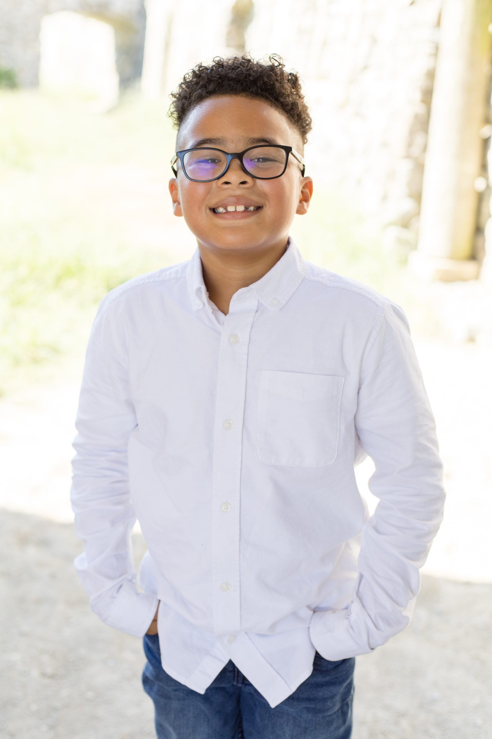 Boy in glasses and white button up shirt poses under bridge at Adriatica Village in McKinney, TX for fall family portrait session. Click to see more from this session by Wisp + Willow Photography Co.
