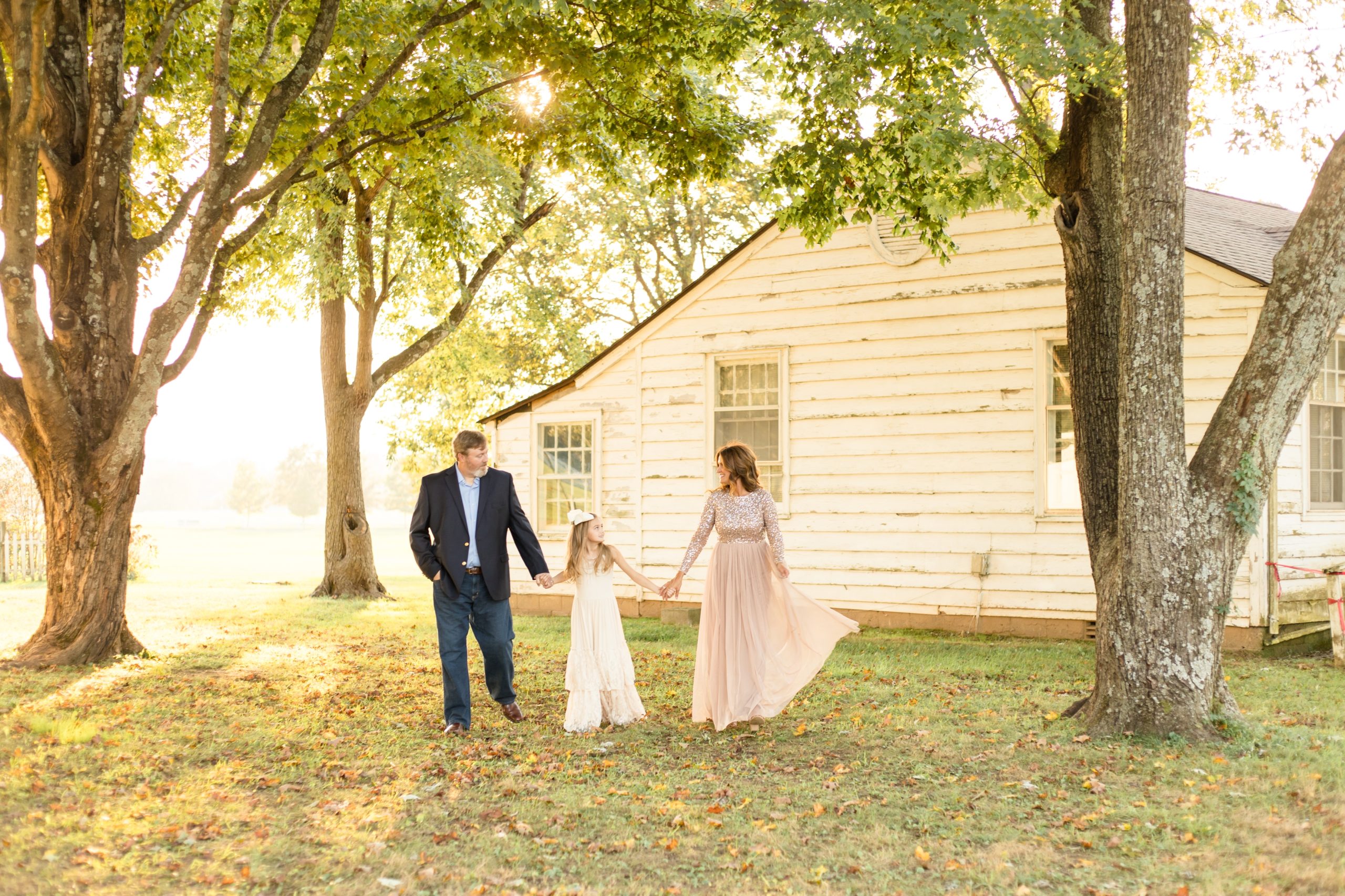 Family walks hand in hand in front of farm house at Harlinsdale farm in Franklin, TN during family portrait session with Wisp + Willow Photography Co.