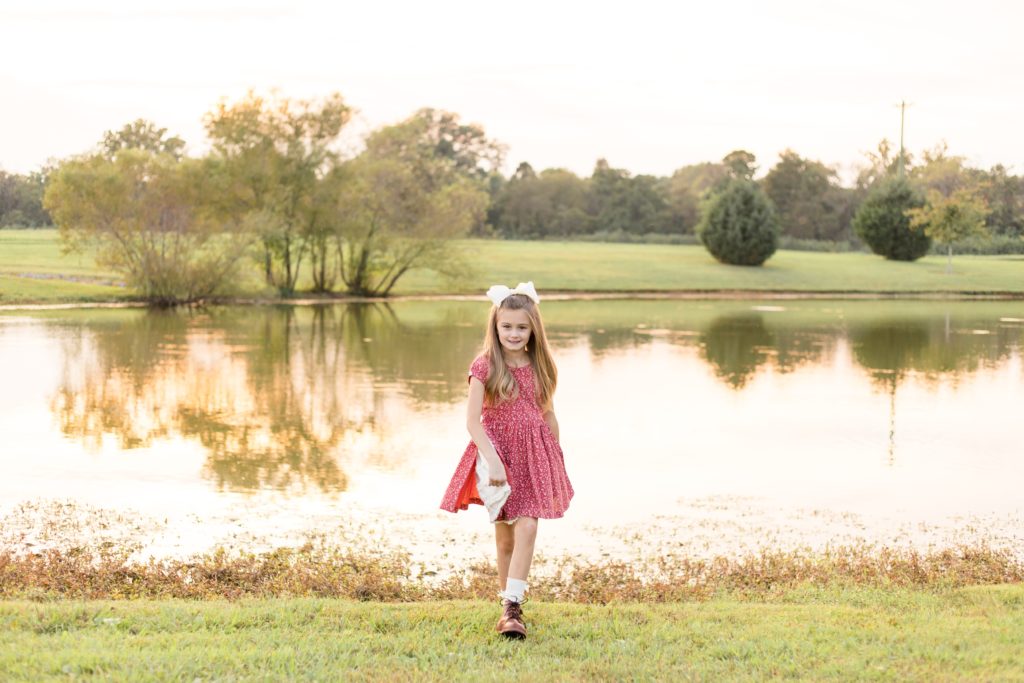 Little girl in red dress walks in front of pond at Harlinsdale Farm in for fall family portrait session with Wisp + Willow Photography Co.