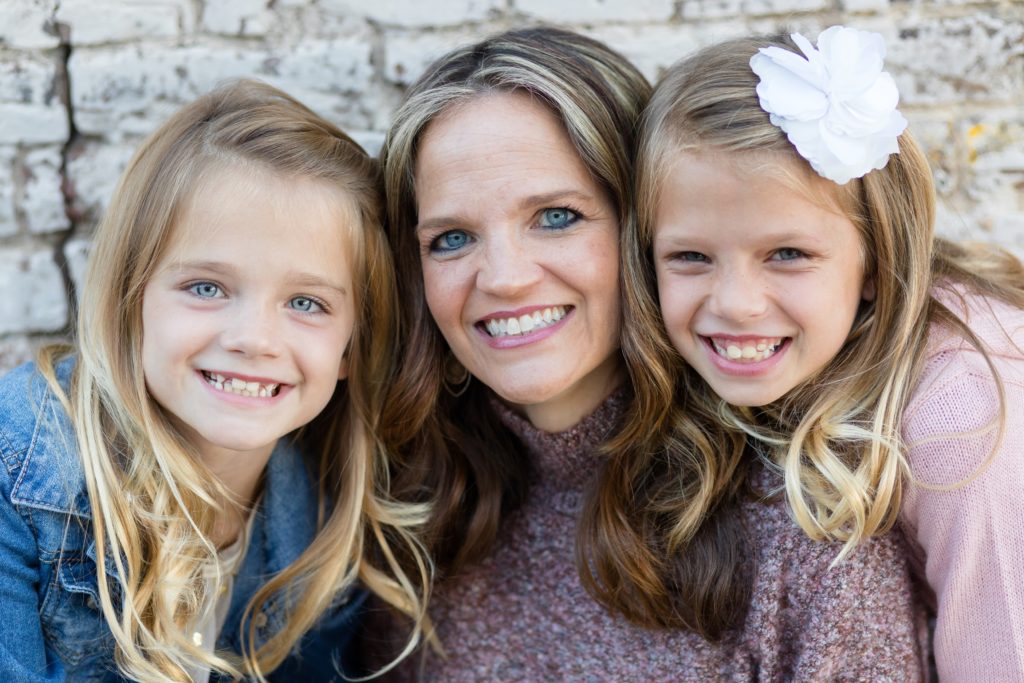 Mom poses with daughters during fall family portrait session with Wisp + Willow Photography Co. in the historic Downtown McKinney Square.