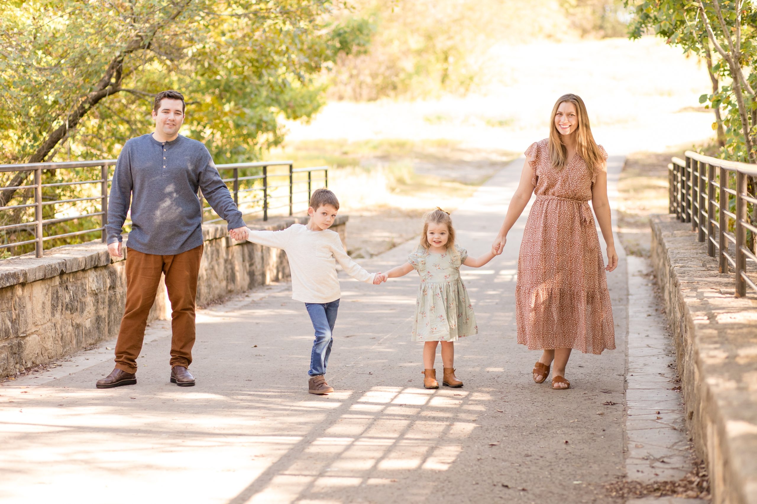 Family of 4 stands hand in hand on bridge during family portrait session at Arbor Hills Nature Preserve with Plano family photographer Wisp + Willow Photography Co. 
