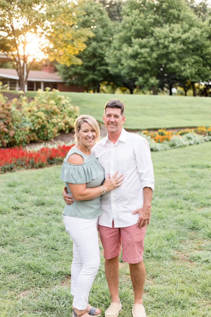 Husband and wife pose for family portrait session in the spring in field with flowers at one of our favorite photography locations in Nashville, TN. Click to see more about why we love Centennial Park on our blog!  