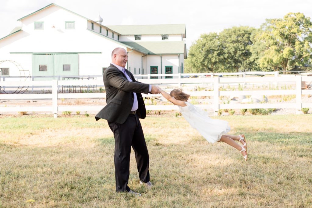 Father in suit swings daughter around during family portrait session in the fall at Harlinsdale Farm in Franklin, TN with Wisp + Willow Photography Co. Click to see more from this session on our blog!
