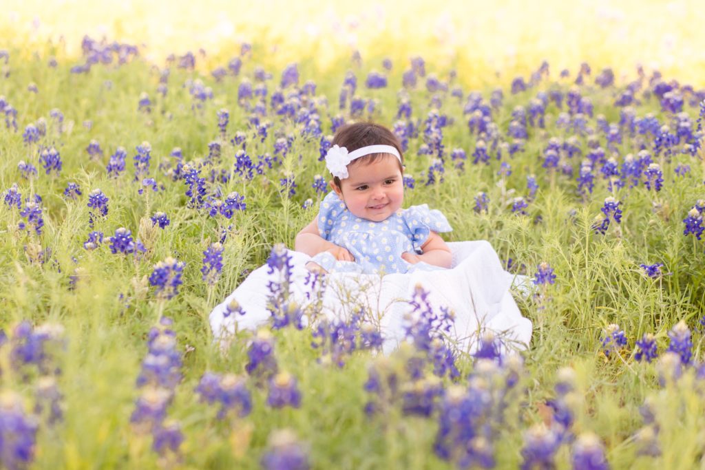 baby girl sits on blanket in field of bluebonnets in plano, tx during mommy and me portrait session with Wisp + Willow Photography Co. Click to see more from this sweet portrait session!