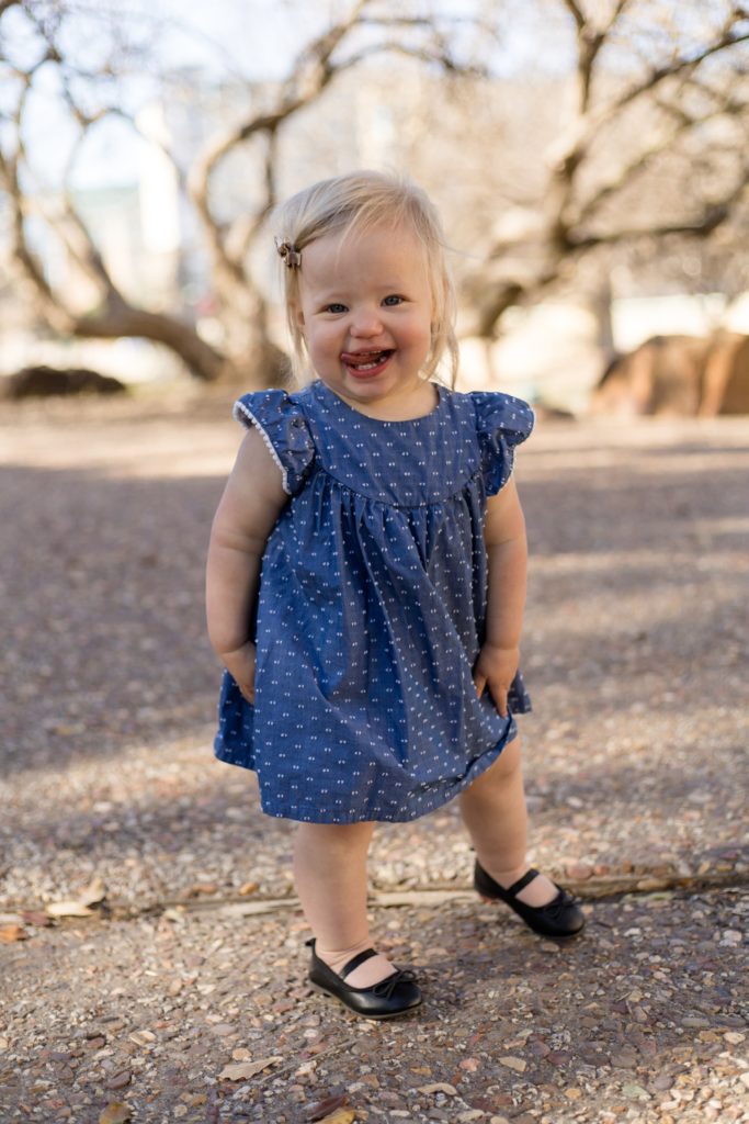 Toddler poses in blue dress during family + maternity session in the spring at Frisco Central Park in Frisco, TX with family photography team Wisp + Willow Photography Co. 