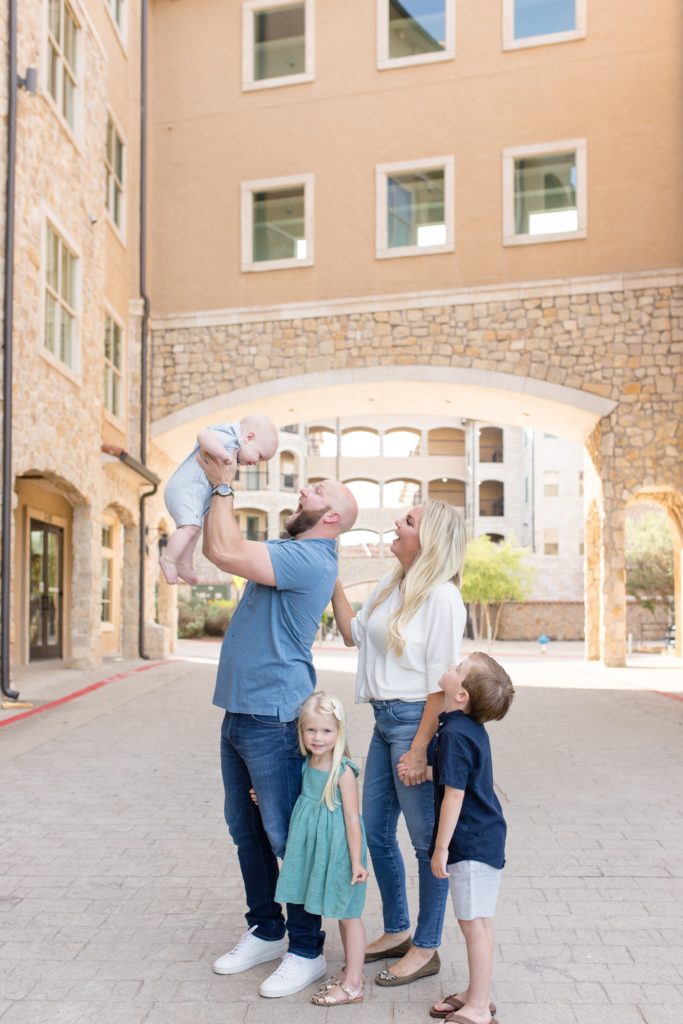 Family of 5 poses under awning at Adriatica Village in McKinney, TX during spring portrait session with family photography team Wisp + Willow Photography Co. Click to read more from this session on the blog!