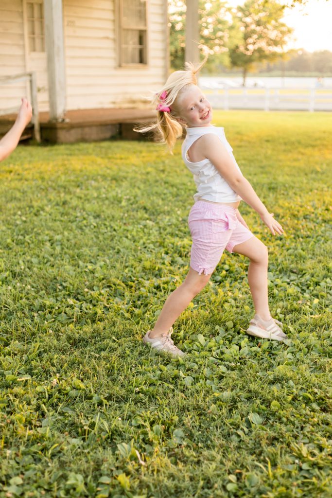 Girl plays in grass in front of old farm house at Harlinsdale Farm in Franklin, TN during mommy and me session with Wisp + Willow Photography Co. Click to see more from this session on our blog now!