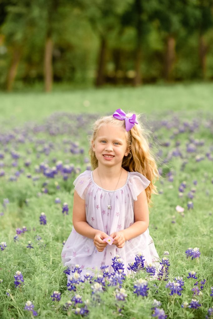 Plano family photographer captures little girl in purple dress in bluebonnet field with family photographer Wisp + Willow Photography Co. 