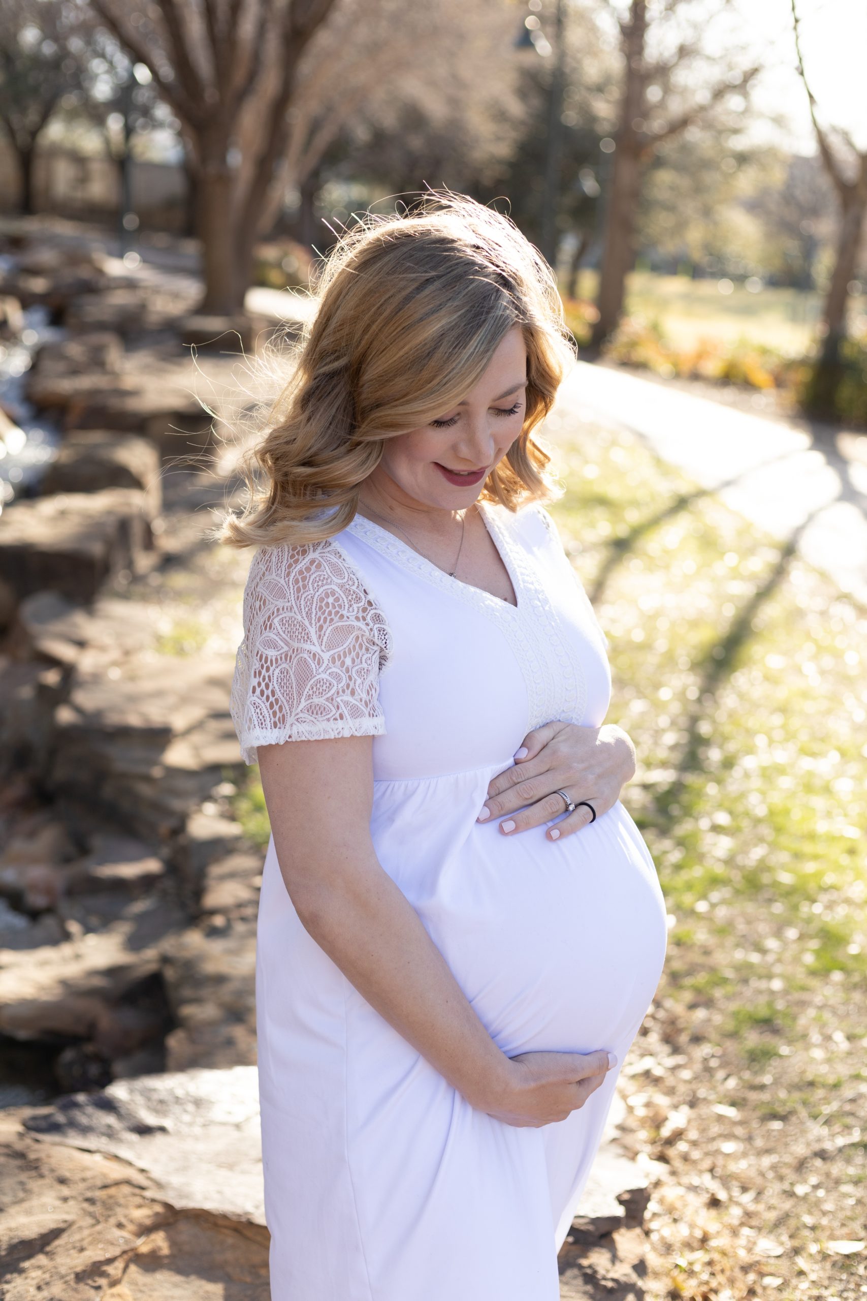 Expecting mom holds pregnant belly in white gown during maternity portrait session at Frisco Central Park with family photographer Wisp + Willow Photography Co. Click to see more from this session live on the blog now. 