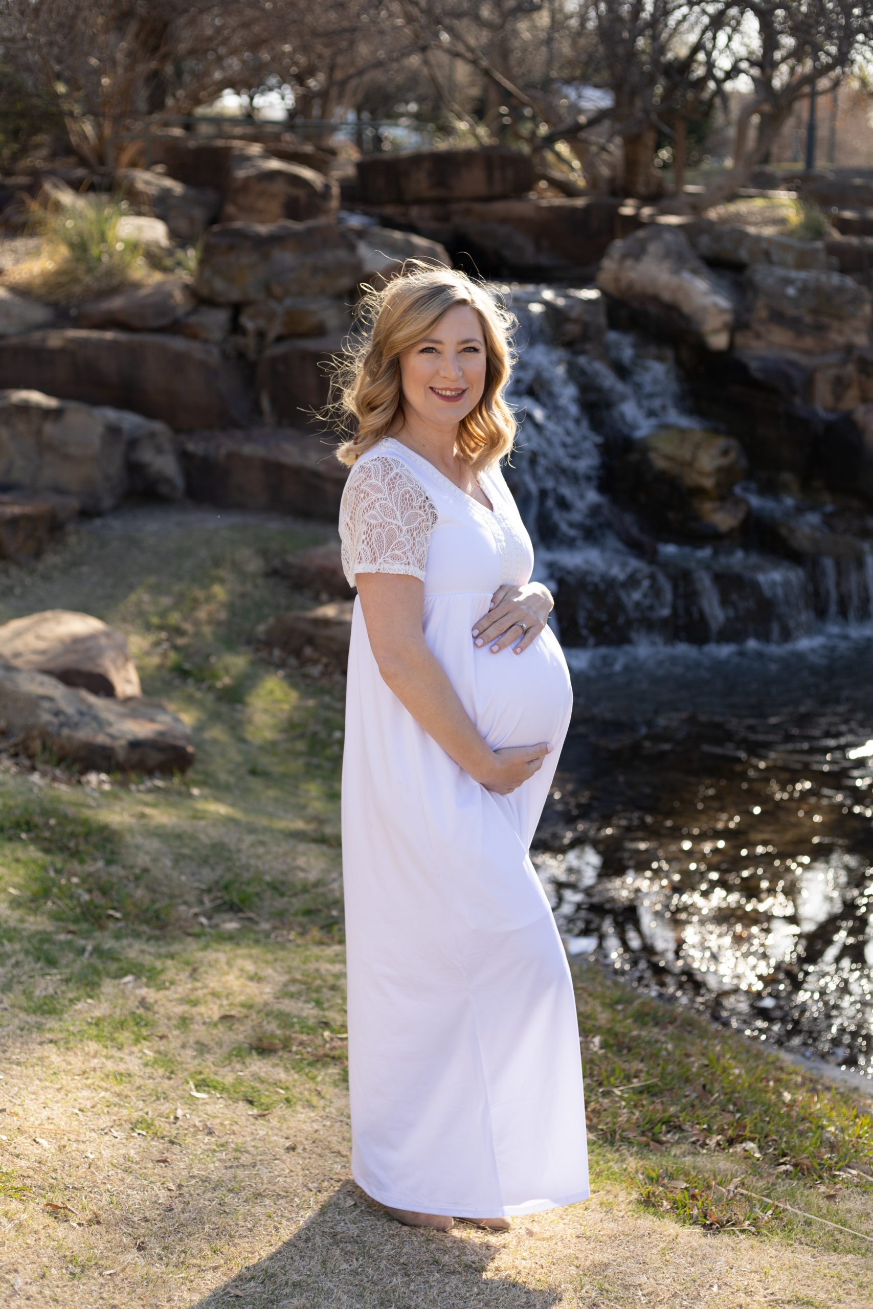 Expecting mom holds pregnant belly in white gown during maternity portrait session at Frisco Central Park with family photographer Wisp + Willow Photography Co. Click to see more from this session live on the blog now. 
