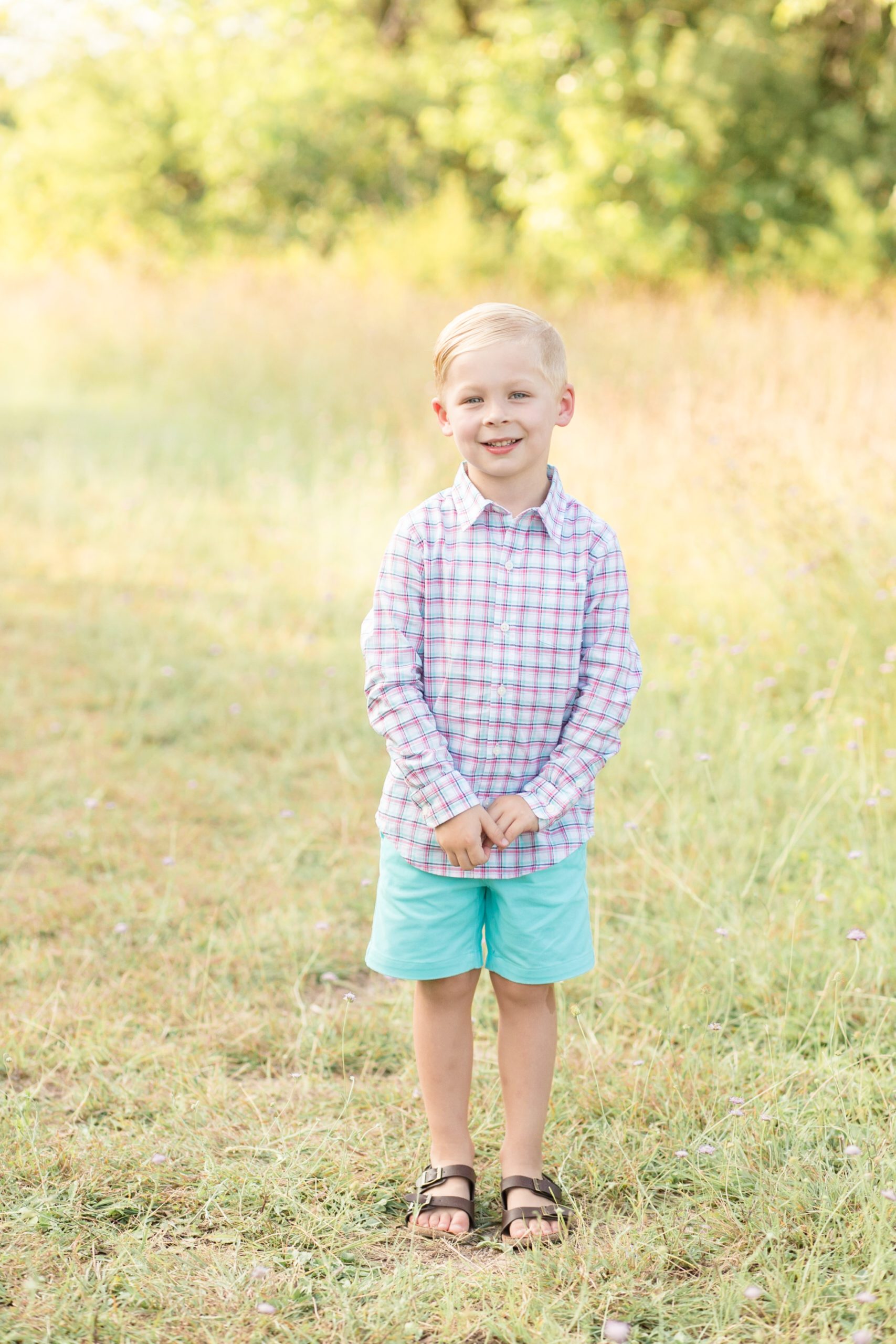 Young boy stands in field of grass for portrait session with mom during the summer at Frisco Commons Park with family photography team Wisp + Willow Photography Co. This session was so precious! Click to see more from this live on the blog now! 