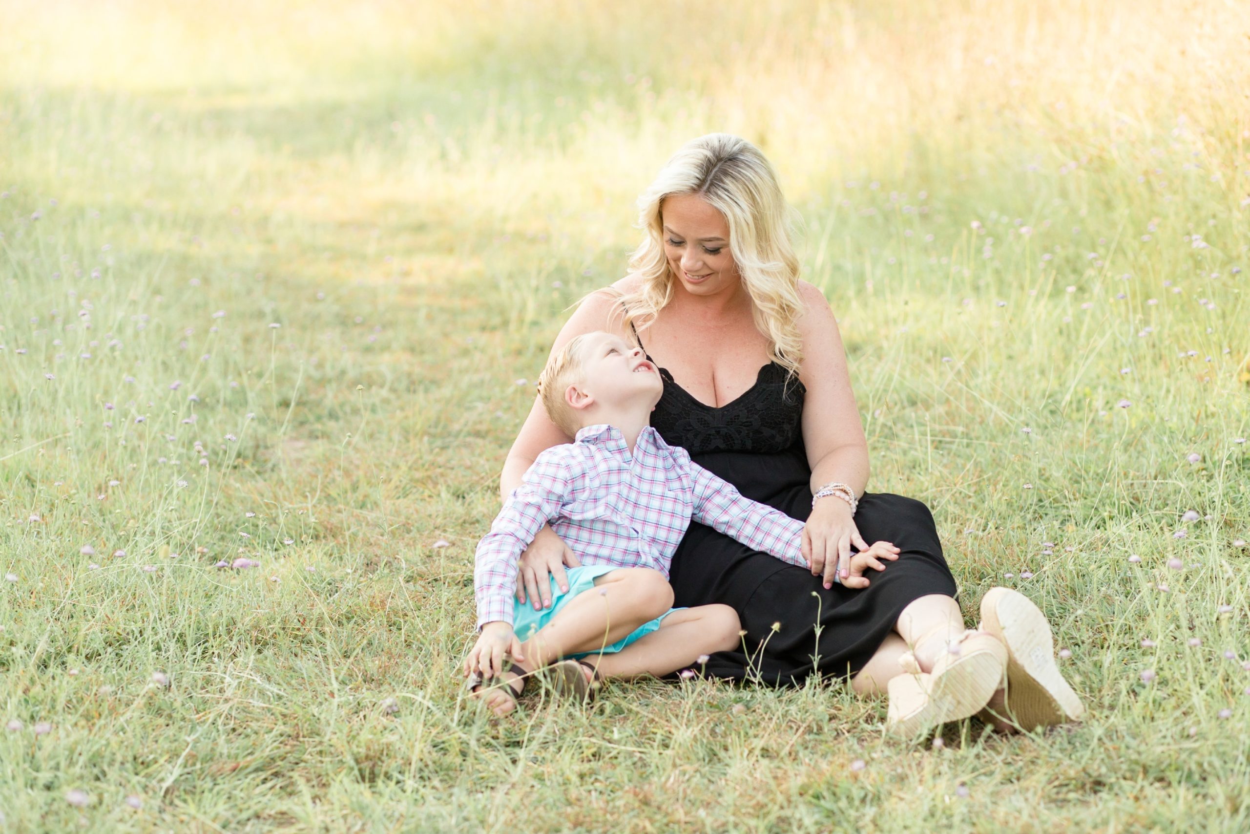 Mom in black dress holds son in grassy field at Frisco Commons Park in Frisco, TX for mommy and me summer portrait session with family photography team Wisp + Willow Photography Co. Click to see more from this adorable session by our associate team on the blog now! 