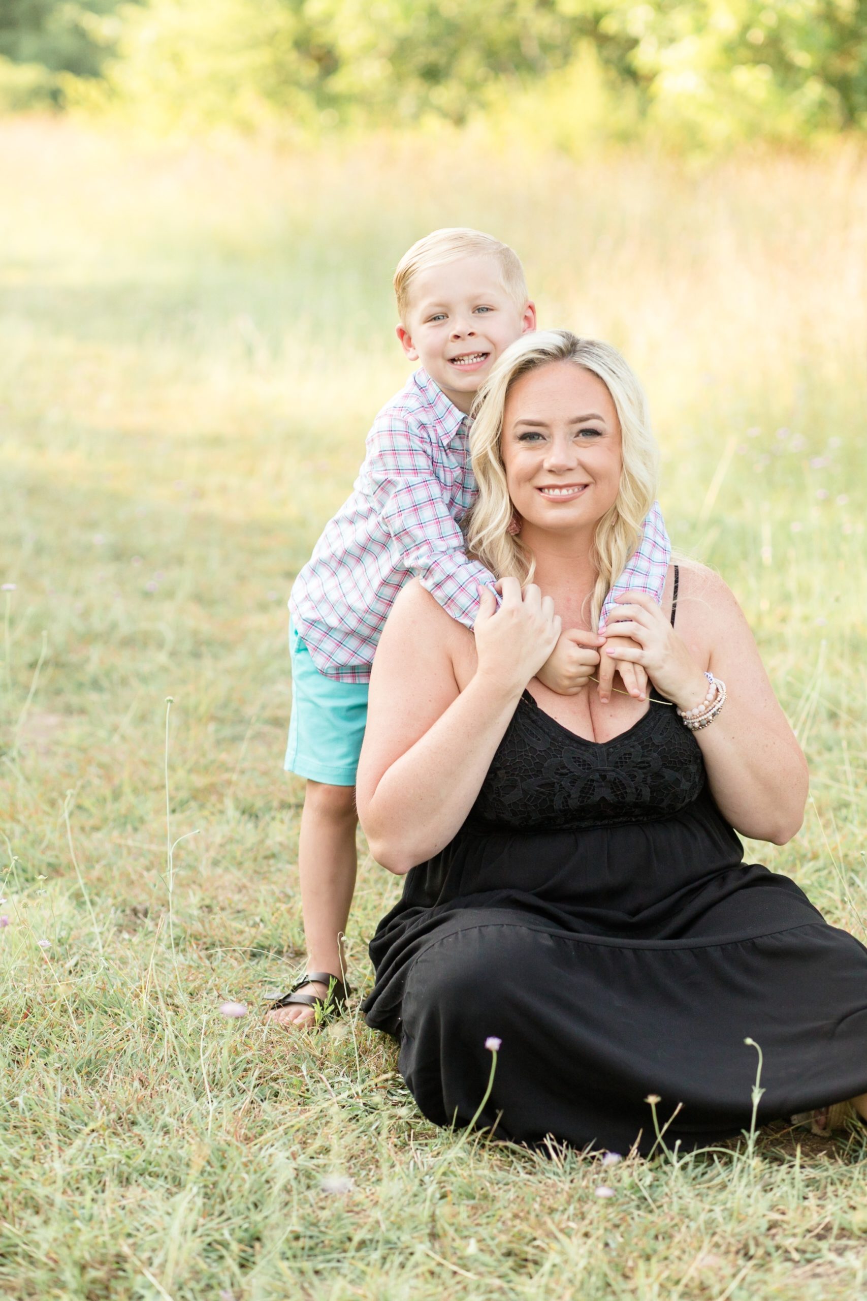 Young boy stands in field and hugs mom of grass for portrait session with mom during the summer at Frisco Commons Park with family photography team Wisp + Willow Photography Co. This session was so precious! Click to see more from this live on the blog now!