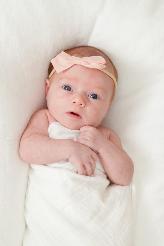 Baby girl in pink bow and white muslin swaddle lays on bed during lifestyle newborn session in family home with family photography team Wisp + Willow Photography Co. This session was so beautiful. Click to see more images from this session live on the blog now! 