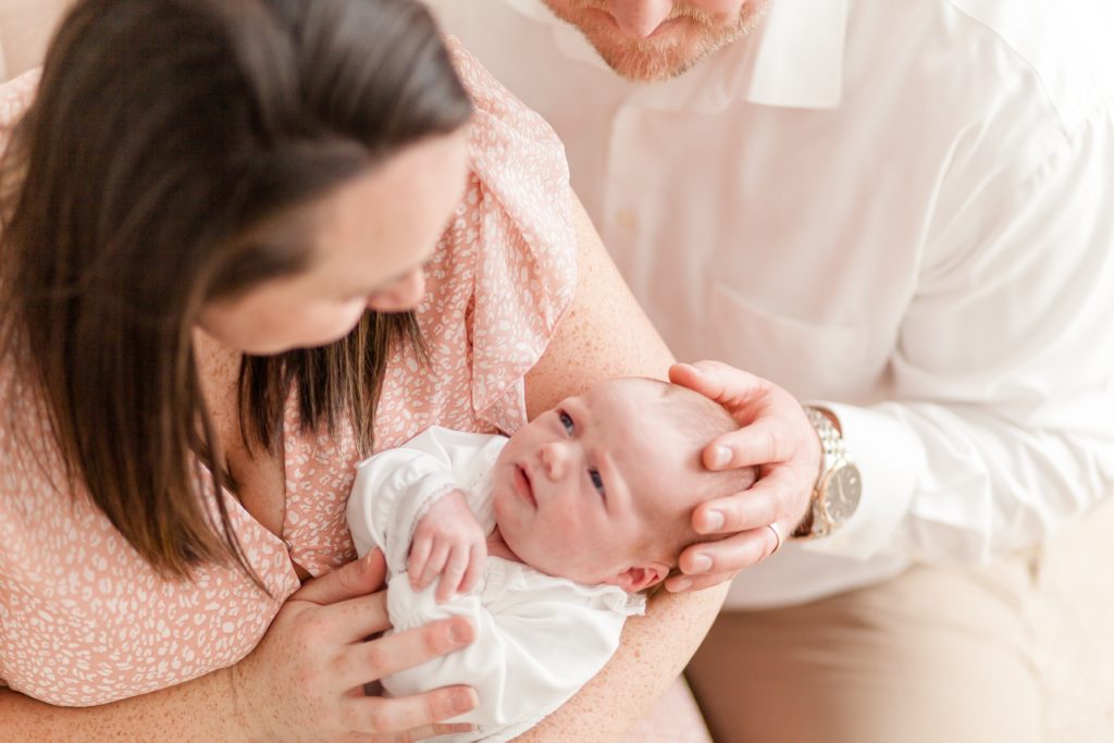 Mom in peach leopard print dress and dad in white button up shirt hold newborn daughter during in home lifestyle newborn session with family photography team Wisp + Willow Photography Co. This session was stunning. Click to see more live on our blog now! 