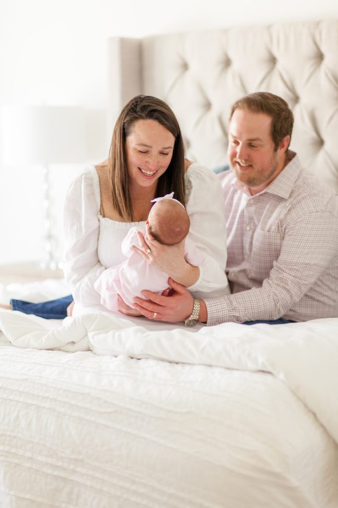 Mom and dad hold baby girl on bed during lifestyle newborn session with family photography team Wisp + Willow Photography Co. Click to see more from this precious session live on the blog now. 