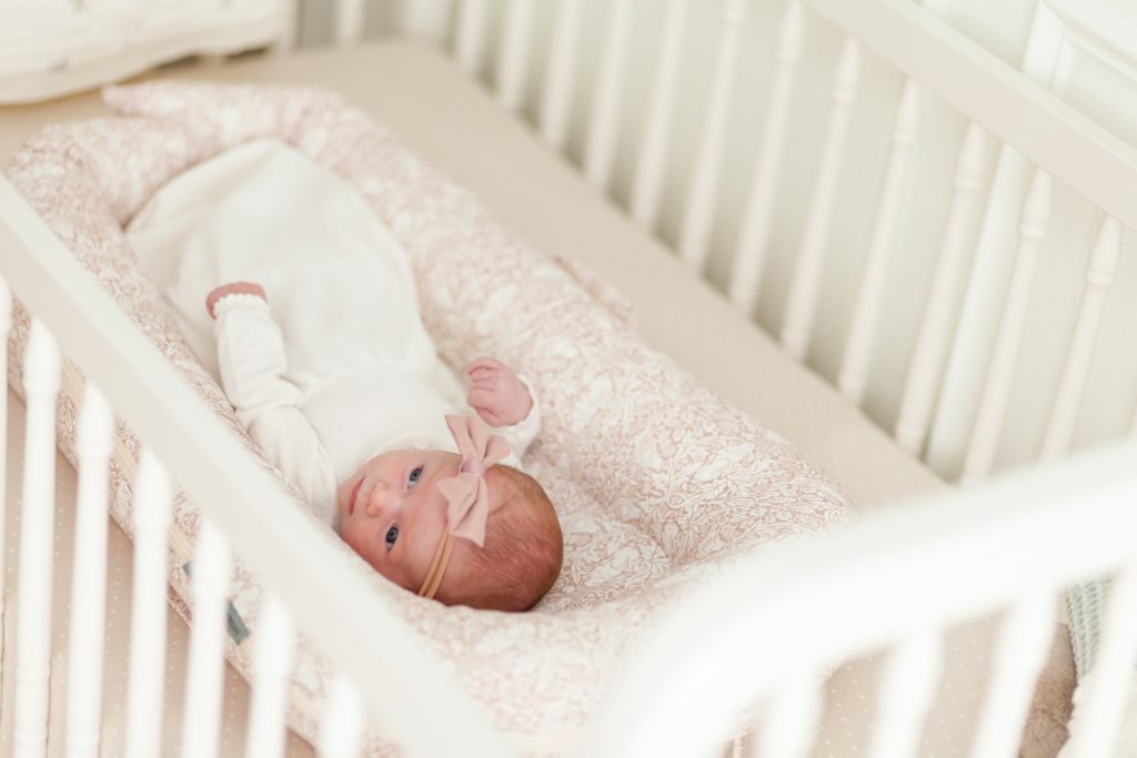 Baby girl lays in crib with pink bow during lifestyle newborn session with associate team wisp + willow photography co. click to see more from this sweet session live on the blog now! 