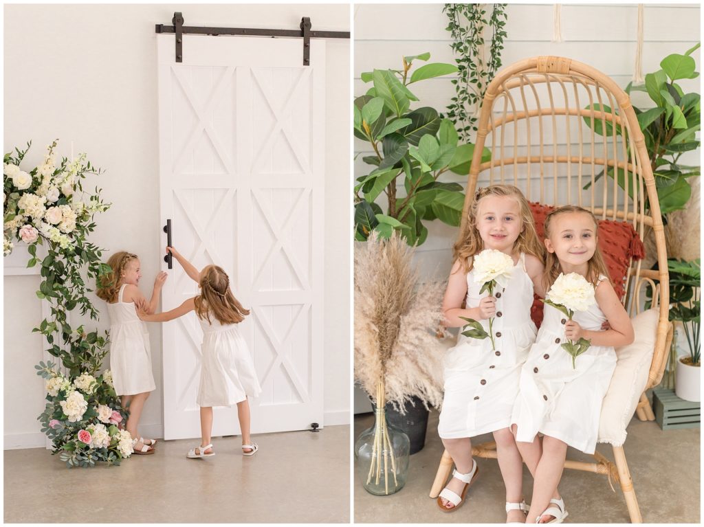 Sisters are pictured playing inside Lemon Drop studios. They are opening a large white door with beautiful greenery and large white flowers to the side. The girls are wearing matching white sleeveless dresses with matching white sandals. The sisters are also seen sitting in an amzing egg chair holding off white flowers.