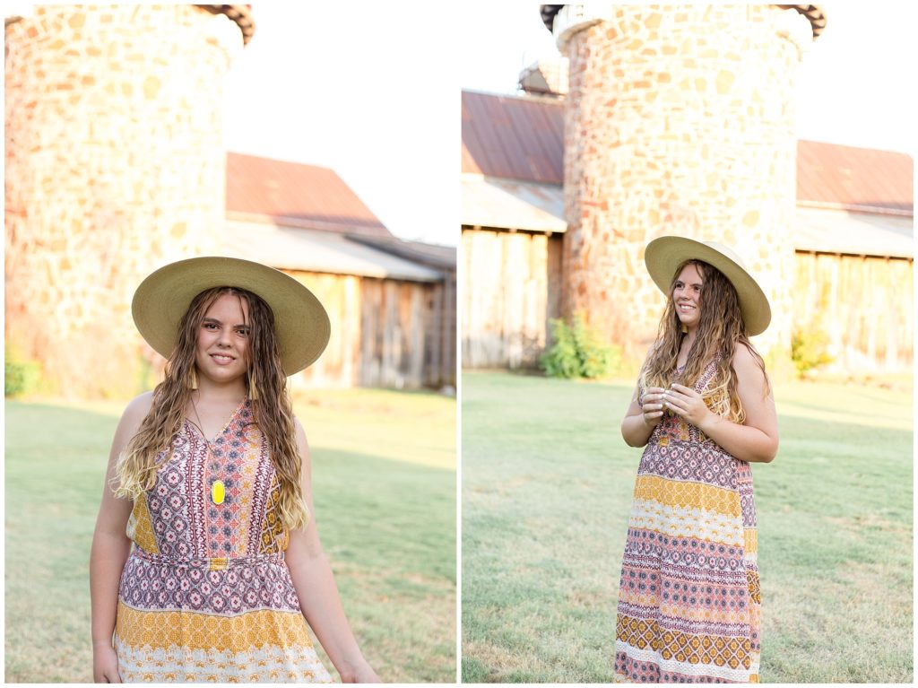The client is standing with an amazing stone and wood rustic building in the background in this Frisco Heritage Center Senior Session. She is wearing a beautiful long, sleeveless multi-colored bohemian style dress with cowboy boots and a wide brim hat, and a long necklace with a bright yellow pendant and dangle fringe earrings.
