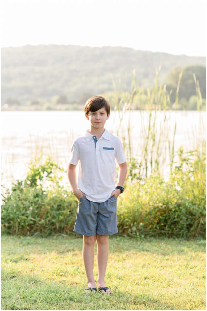 So is standing just in font of an amazing lake. He is dressed in a white short sleeve polo and blue shorts.