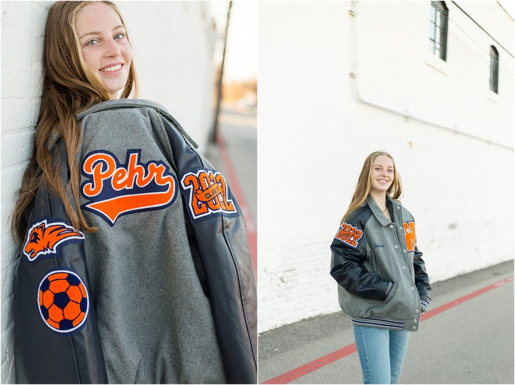 This high school senior is wearing her grey, blue and orange letterman jacket. 