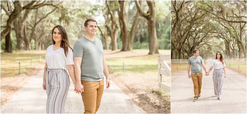 Husband and wife are walking hand in hand beneath a gorgeous archway of trees. Wife is wearing a short sleeve white shirt and a multi-colored striped pants. Husband is wearing a sage green short sleeve shirt and brown pants.
