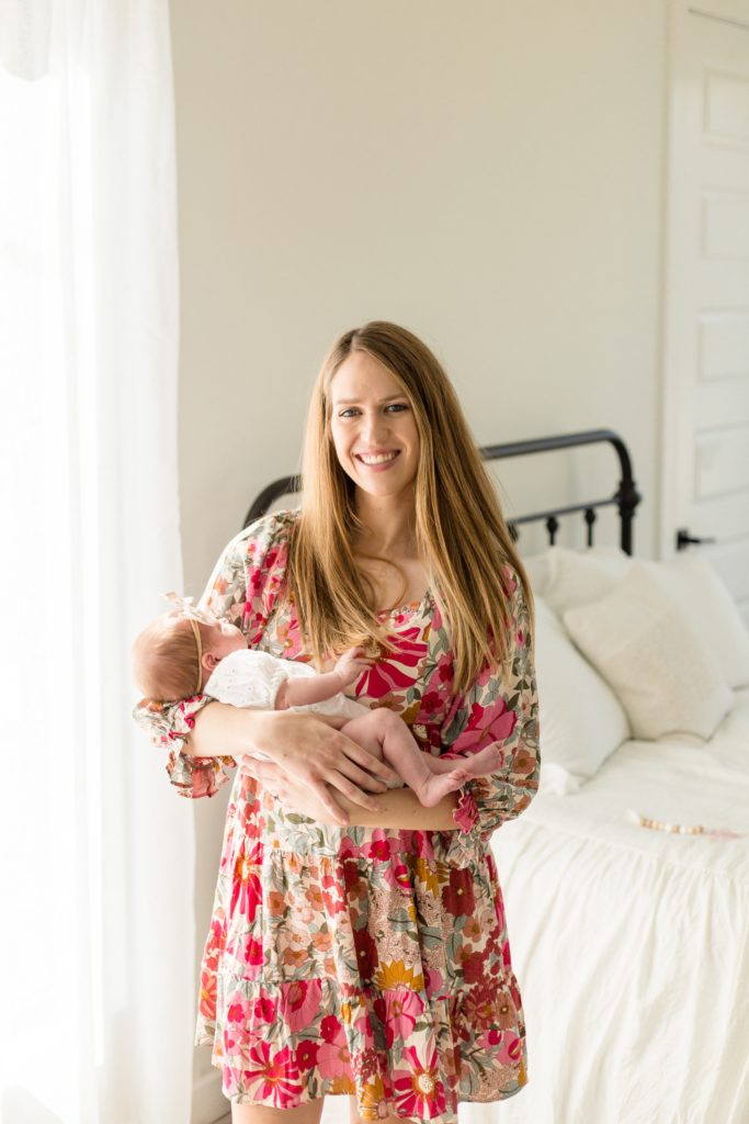 Mom in floral dress holds baby girl for picture during lifestyle newborn session with Wisp + Willow Photography Co. Click to see more from this McKinney session live on the blog now!