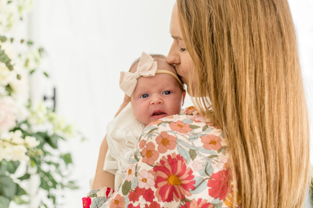 Mom in floral dress kisses baby girl on forehead during sweet mommy and me lifestyle newborn session in the spring at Lemon Drop Studios in McKinney, Texas with Wisp + Willow Photography Co. Click to see more from this lovely session live on the blog now! 
