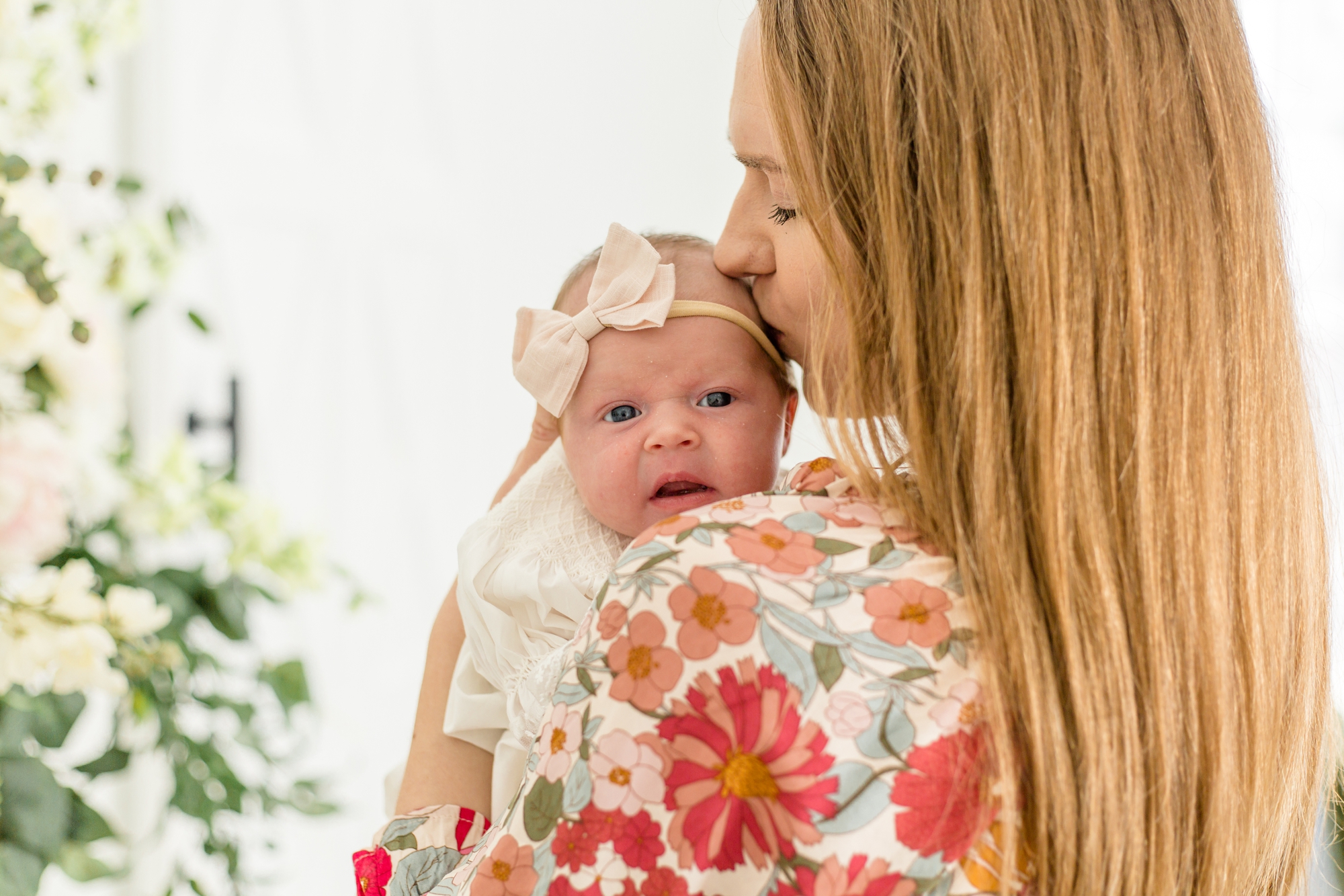 Mom in floral dress kisses baby girl on forehead during sweet mommy and me lifestyle newborn session in the spring at Lemon Drop Studios in McKinney, Texas with Wisp + Willow Photography Co. Click to see more from this lovely session live on the blog now!