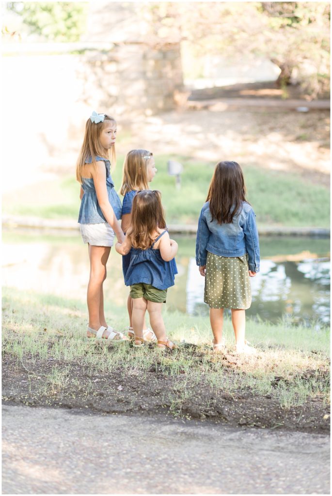 4 girls in denim outfits stand in front of pond together in Frisco Central Park during extended family photo session. 