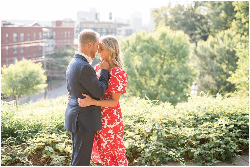 Engaged couple in blue suit and red and white dress hold each other close overlooking Richmond, VA during photo session with Wisp + Willow Photography Co. 