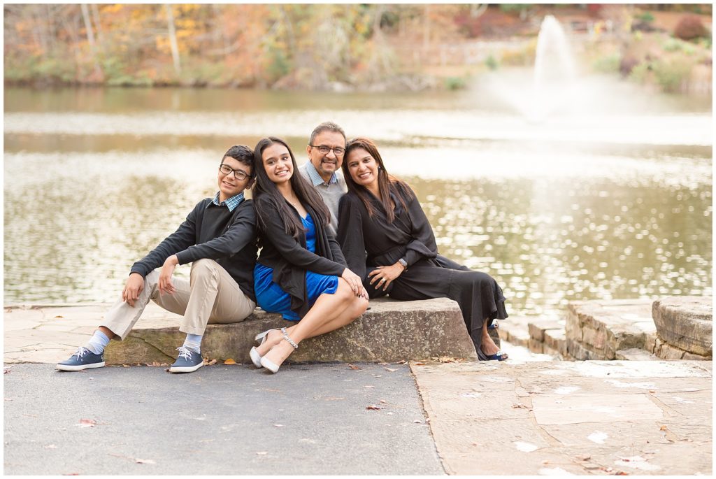 Family of 4 sit on large rock in front of lake in Sims Lake Park during fall family photo session with Wisp + Willow Photography Co. 