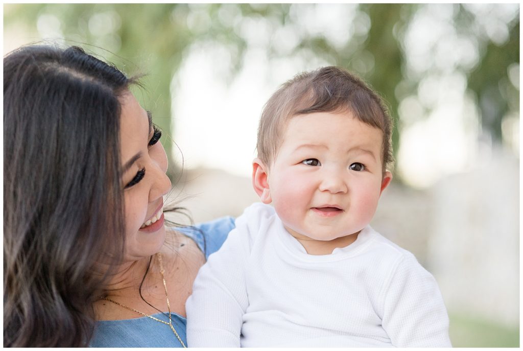 8 month old baby boy smiles while mom looks on happily!  Wisp + Willow Photography Co. are McKinney, TX family photographers.