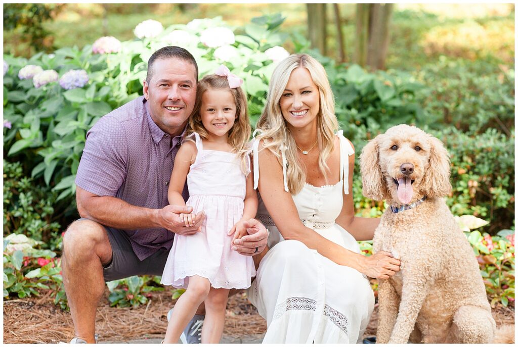 Azalea Garden Family Photography session in Raleigh, NC with family of 3 and their goldendoodle wear coordinating outfits of white, pink, and purple.