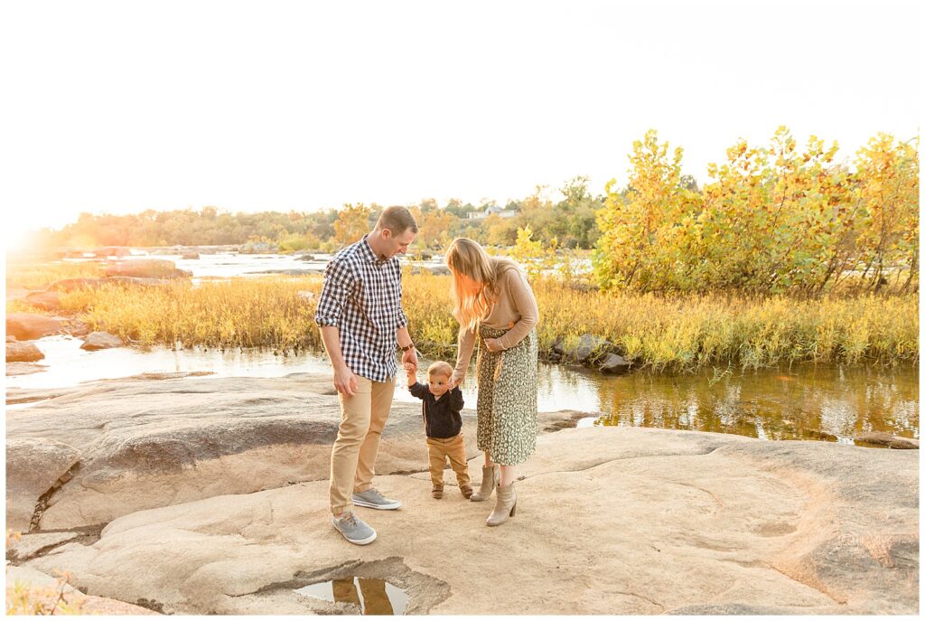Richmond family photographer, Wisp + Willow Photography Co, captures family of 3 as they walk on the rocks of Belle Isle and Mom holds belly to share baby announcement news.