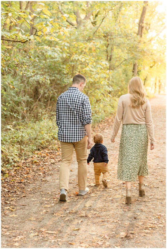 Family of 3 walk on a path filled with trees as they walk away from the camera of Richmond family photographer, Wisp + Willow Photography Co.
