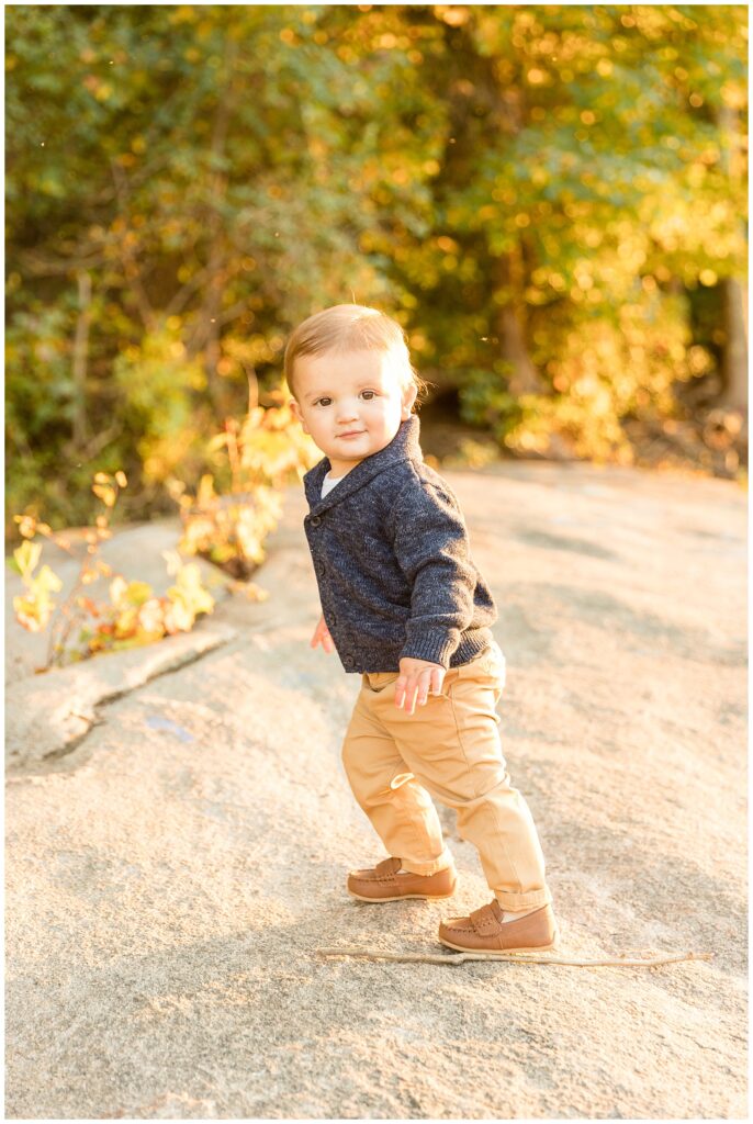 Toddler boy walks up the rocks of Belle Isle as Richmond family photographer, Wisp + Willow Photography Co. capture moment of little boy in blue sweater and khaki pants.
