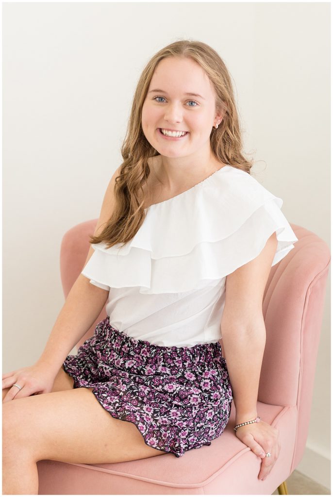 Happy 16th birthday portraits taken at studio in McKinney, TX at Lemon Drop.  Girl sits in blush chair and wears a white dressy blouse with purple floral skirt.  See portrait live on Wisp + Willow Photography Co. blog now!