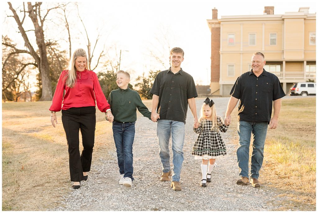 Golden hour lighting comes from behind family walking picture on gravel driveway during family photography session with Wisp + Willow Photography Co.