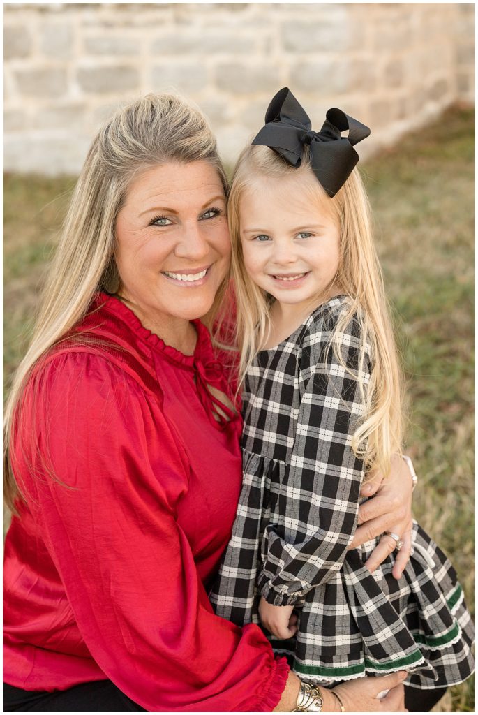Mother daughter smile for Nashville family photographer, Wisp + Willow Photography Co. as mom wears a bright red blouse and daughter wears a black and white checkered dress with black bow.