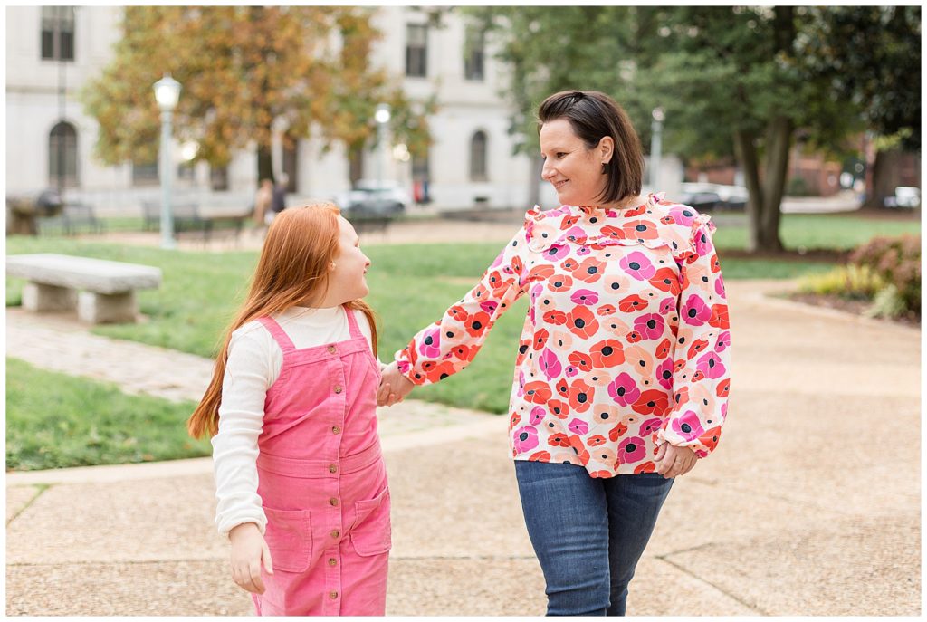 Mom and daughter walk through downtown Raleigh smiling at each other, wearing bright pink and floral colors for their family session.  